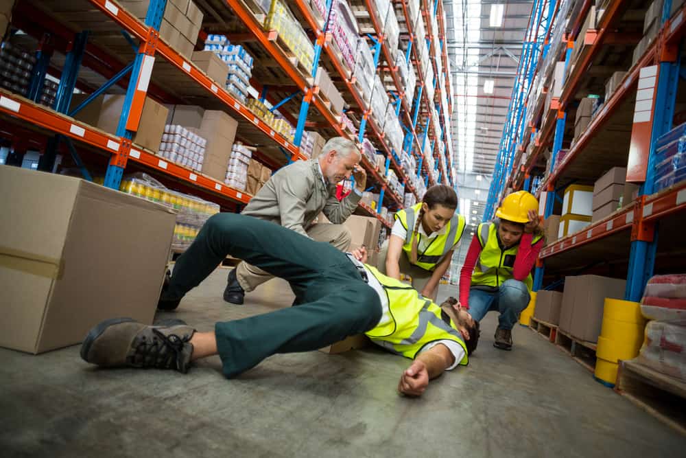 colleagues gathered around a worker who has had an accident at work in a warehouse