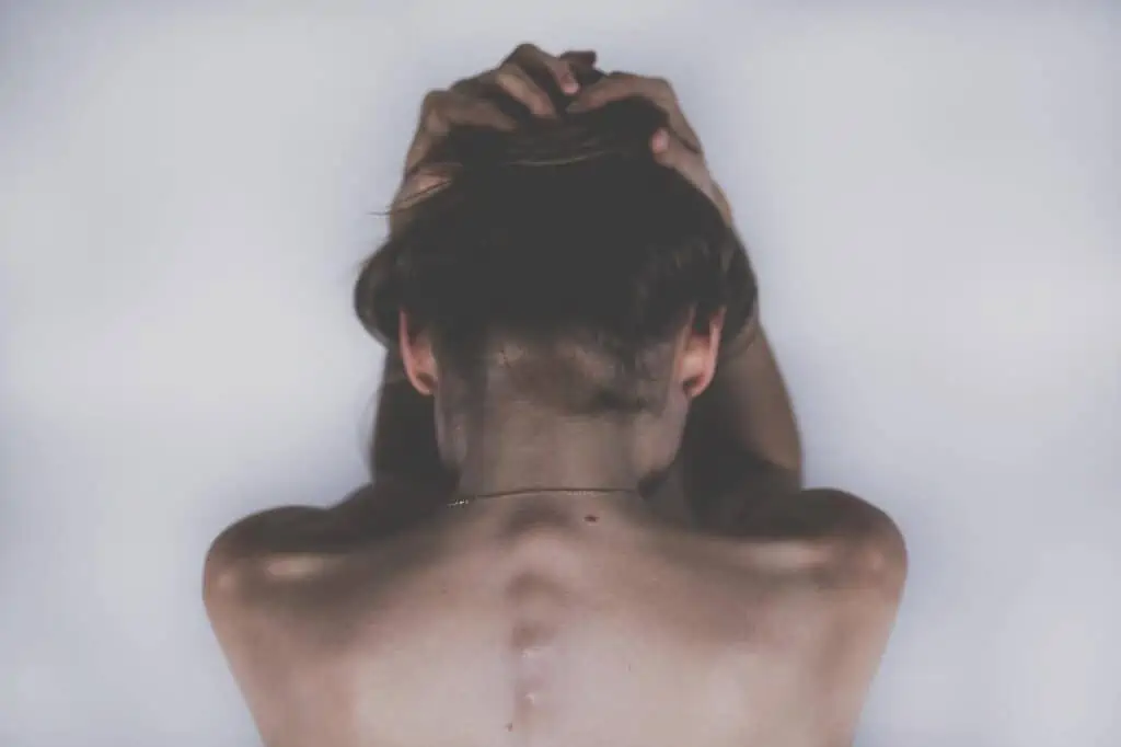 whiplash - woman facing a wall holding her hands in pain